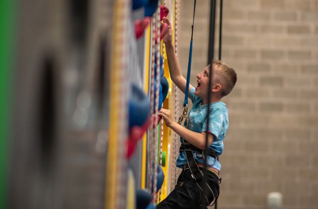 Young boy excitedly climbing up an indoor climbing wall