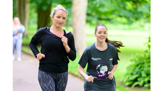 Two women jogging through the park, smiling