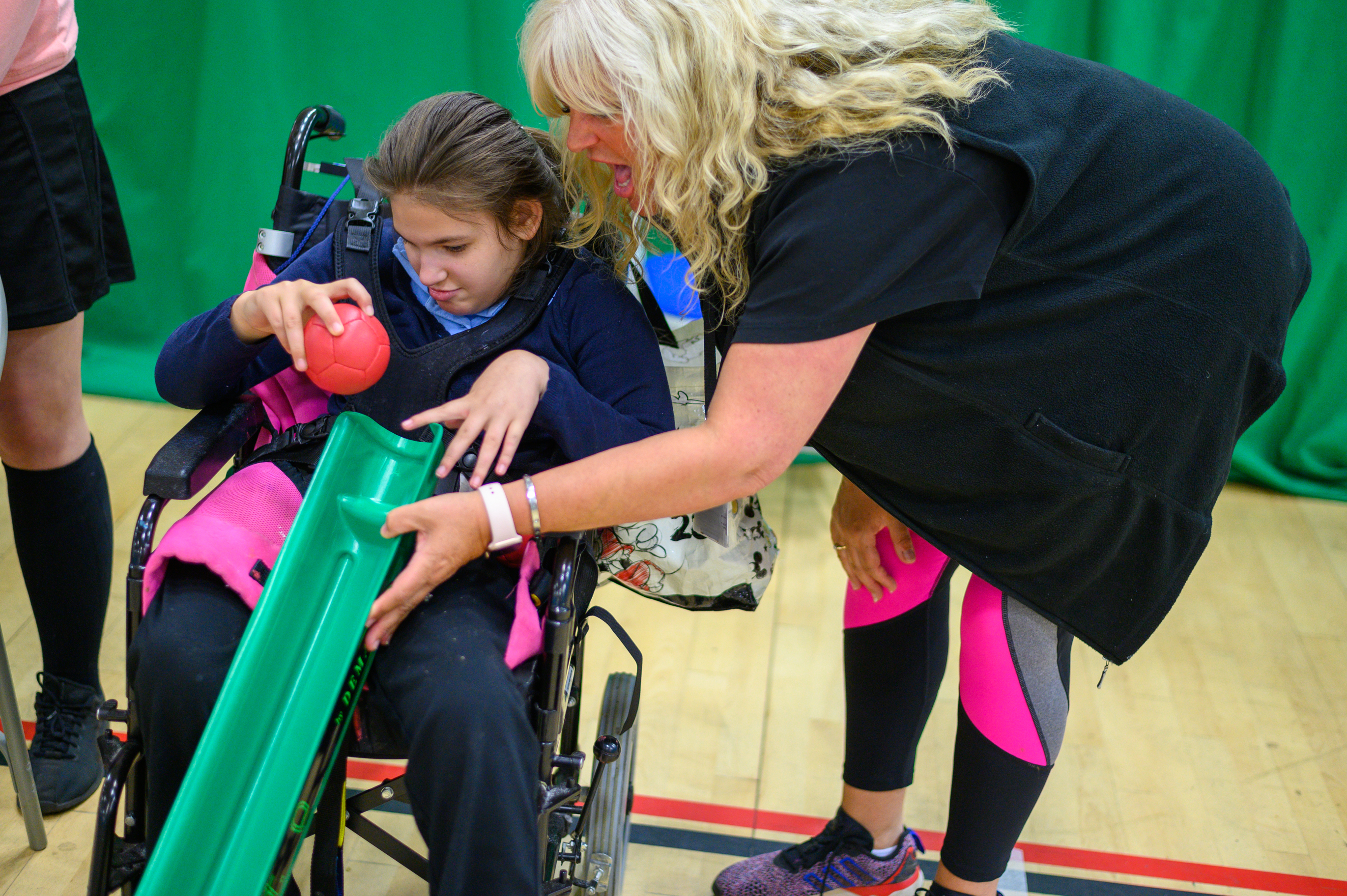 Woman helping a girl in a wheelchair play boccia using a ramp