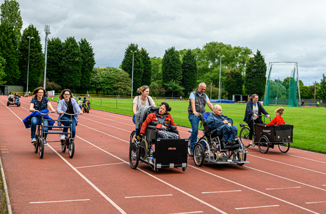 Many people on various types of bike cycling around an athletics track