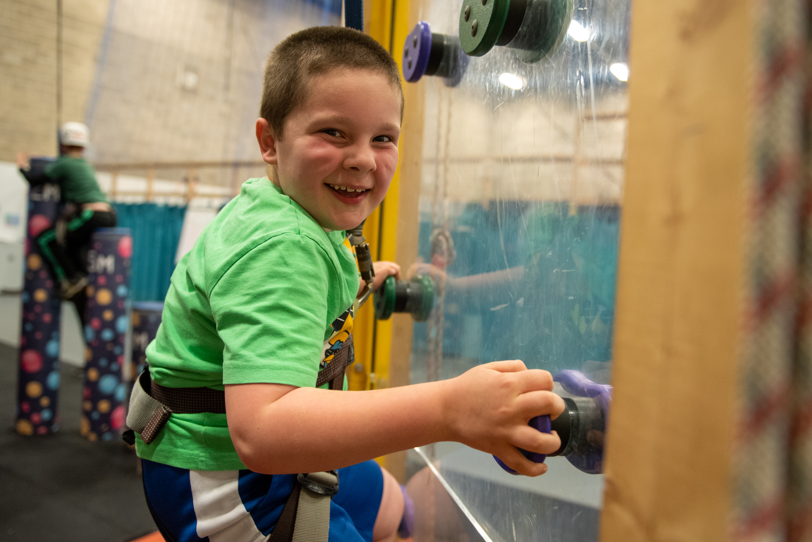 Young boy climbing up an indoor climbing wall smiling at the camera
