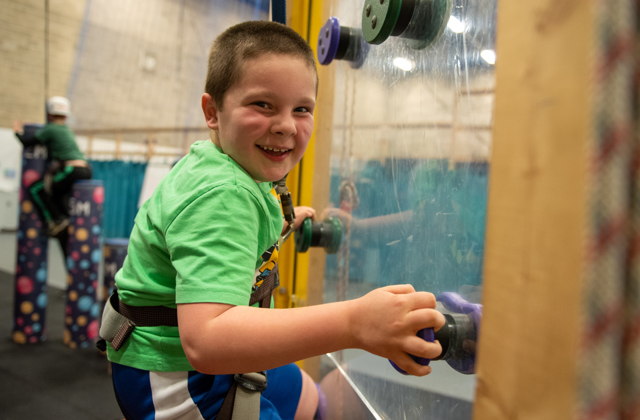 Young boy climbing up an indoor climbing wall smiling at the camera