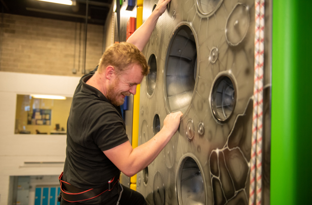 Man smiling whilst climbing up an indoor climbing wall
