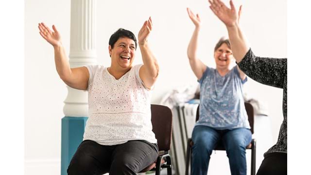 Two women smiling in a chair based exercise class
