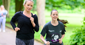 Two women jogging through the park, smiling