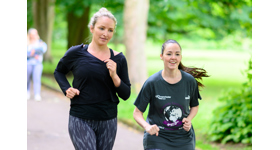 Two women jogging through the park, smiling