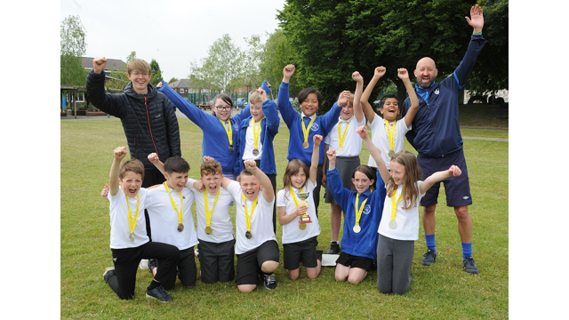 Group of children wearing medals, with two adults all cheering whilst punching the air