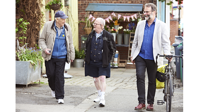 Three older adults walking and talking along a pavement, one is pushing a bike.