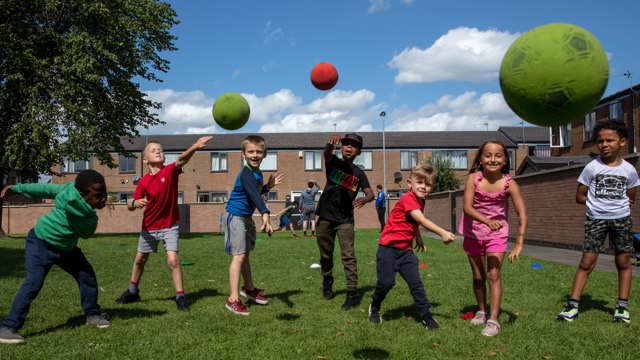 Group of young people in a residential area smiling and throwing balls in the direction of the camera